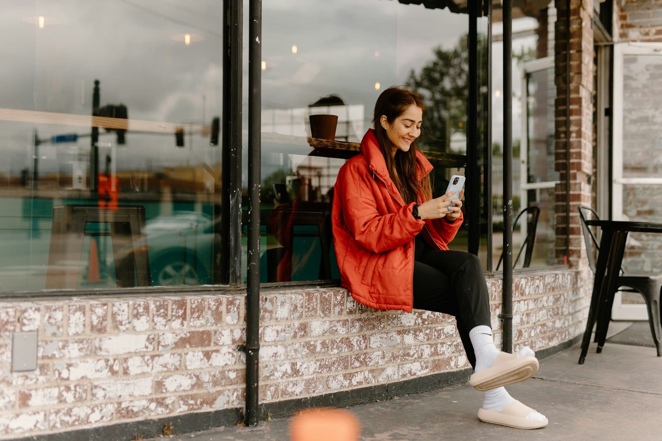 A young woman smiling at her phone outside a café